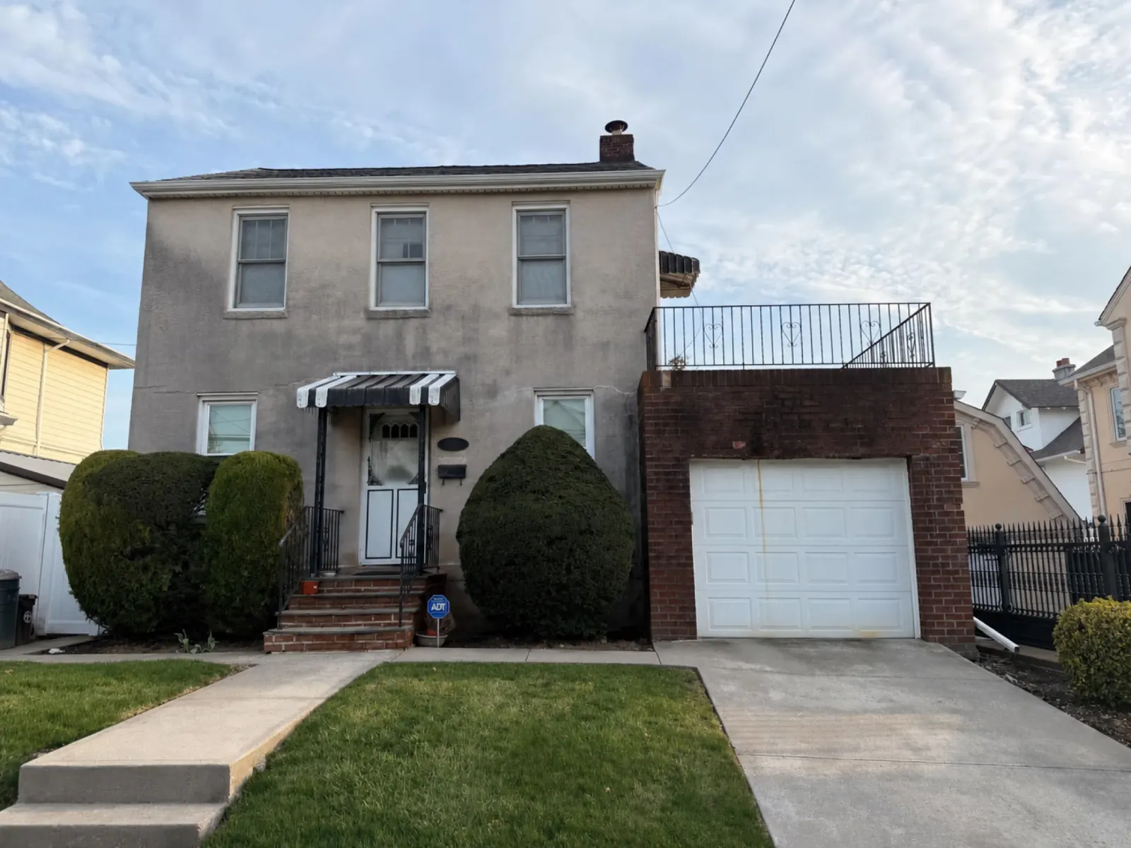 A two-story Whitestone house with a brick garage and clipped shrubs.